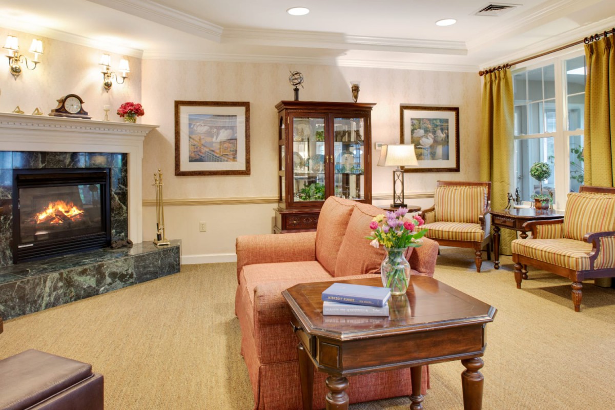 A cozy living room with a sofa, table, and fireplace, adorned with artwork and a vase of flowers.