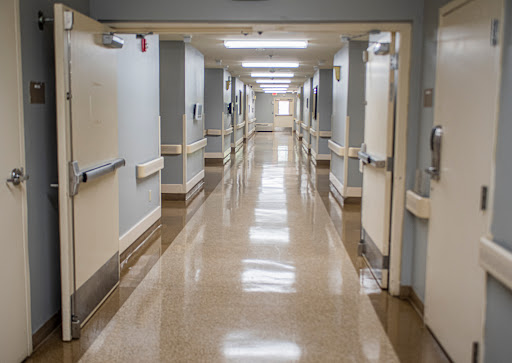 A long, clean corridor within a hospital, featuring doors on either side and bright overhead lighting.