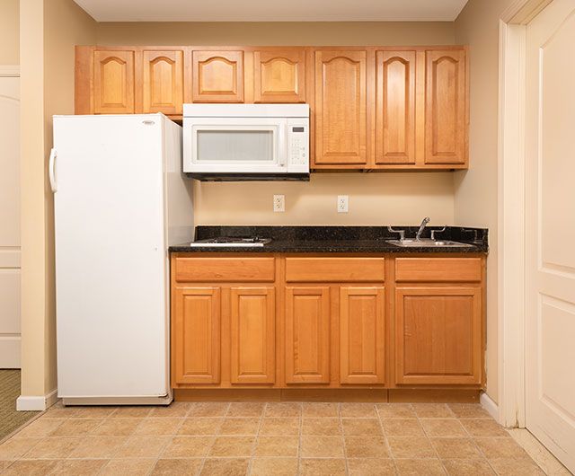 A compact kitchen with wooden cabinets, a refrigerator, microwave, and sink.