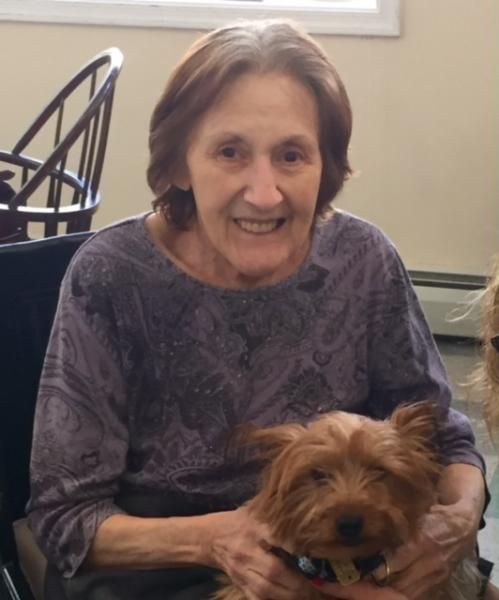 A woman smiling while holding a small dog indoors.