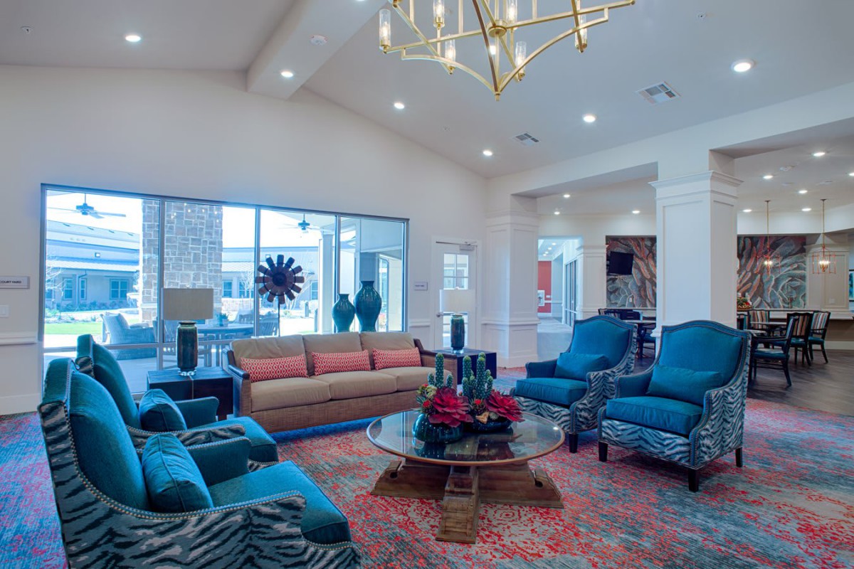 A spacious living room with blue chairs, a sofa, and a central coffee table under a modern chandelier.
