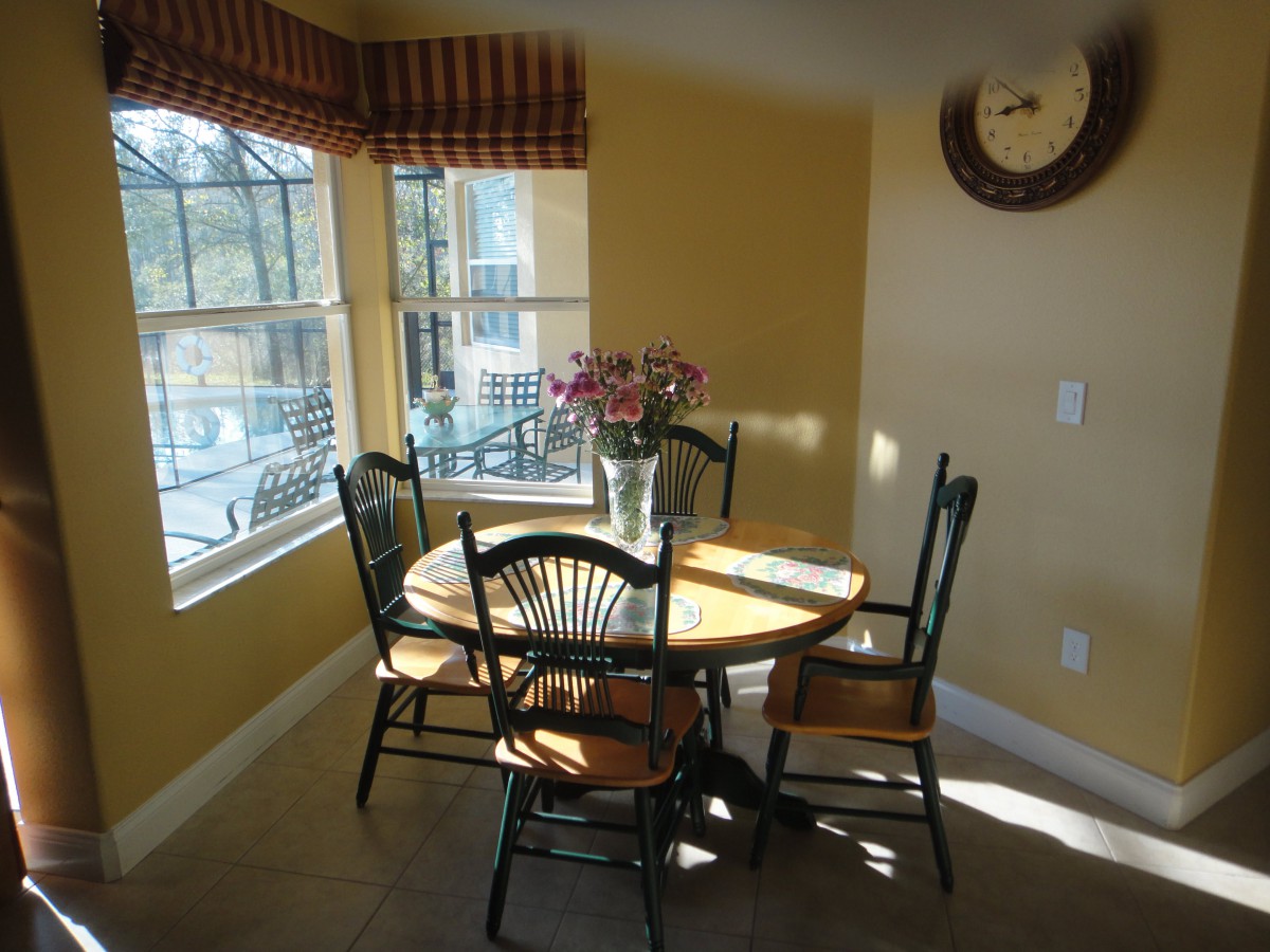A cozy dining area with a round table and chairs, bathed in sunlight streaming through the windows.