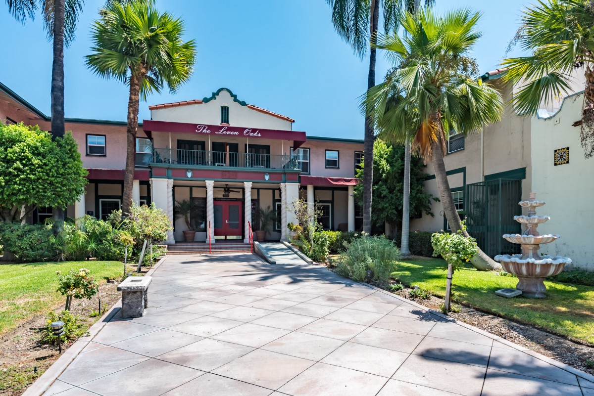 A large mansion with a spacious driveway, surrounded by palm trees and a well-maintained garden.