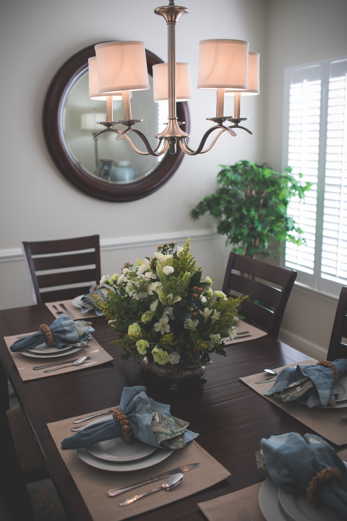 A neatly arranged dining room table with floral centerpiece, lit by an elegant chandelier.