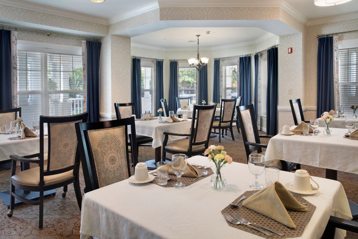 An elegant dining room with neatly arranged tables and chairs, decorated with fine table settings and draped windows.