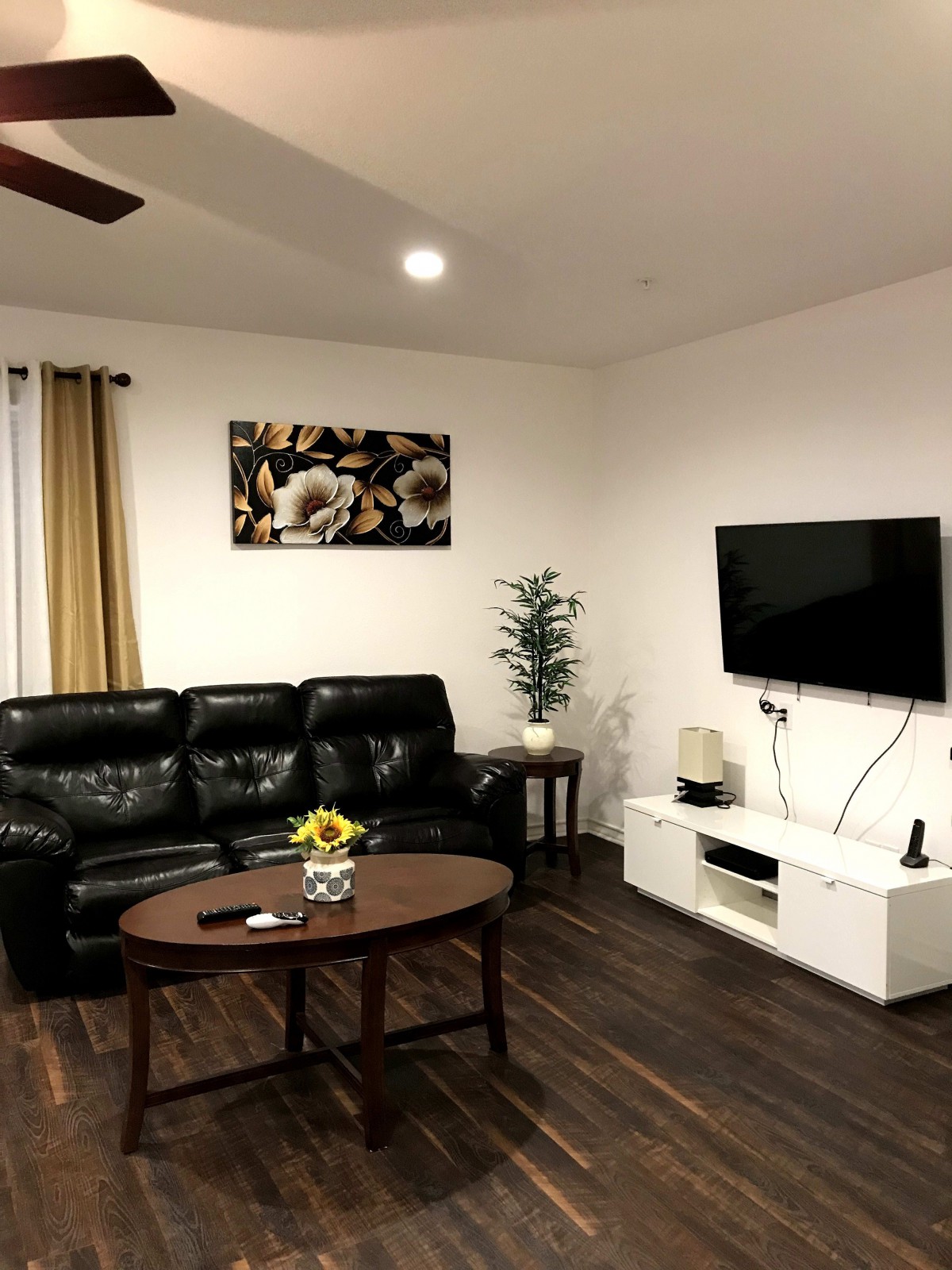 A cozy living room with a black leather sofa, wall-mounted television, and a wooden coffee table.