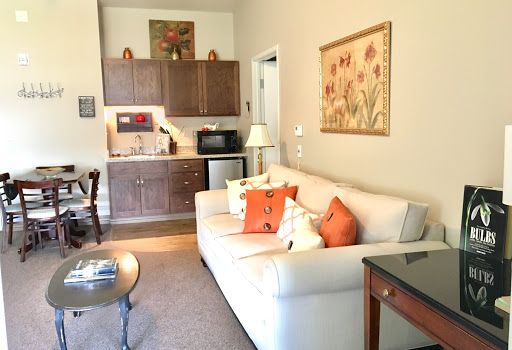 A cozy living area featuring a white sofa with colorful pillows, a small kitchenette, and decorative artwork.