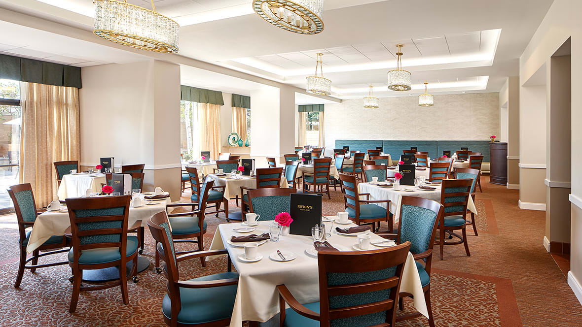 A spacious and elegantly decorated restaurant dining room with neatly set tables and wooden chairs.