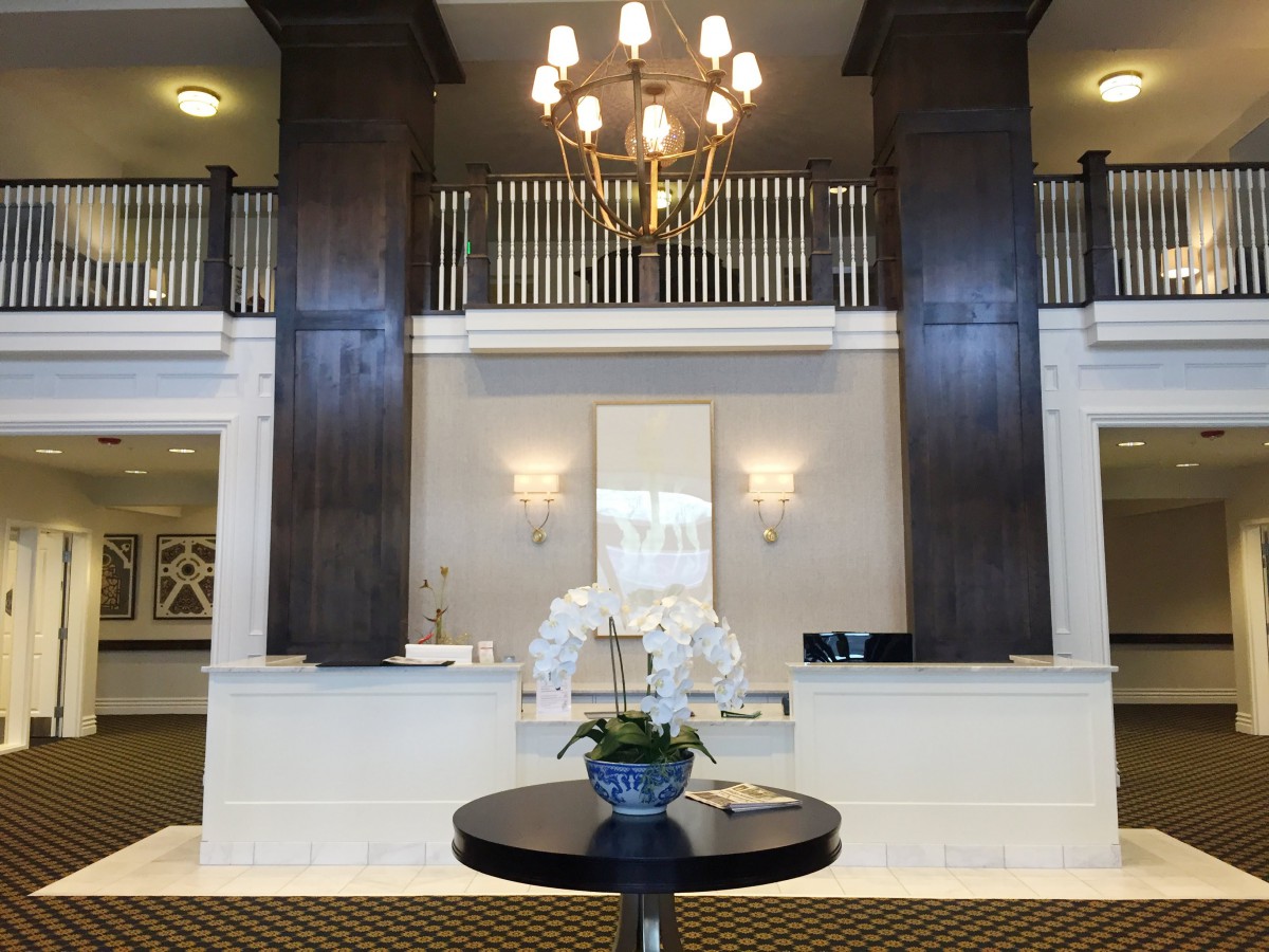 A stylish hotel lobby with a reception desk and elegant chandelier, featuring a floral arrangement on a central table.