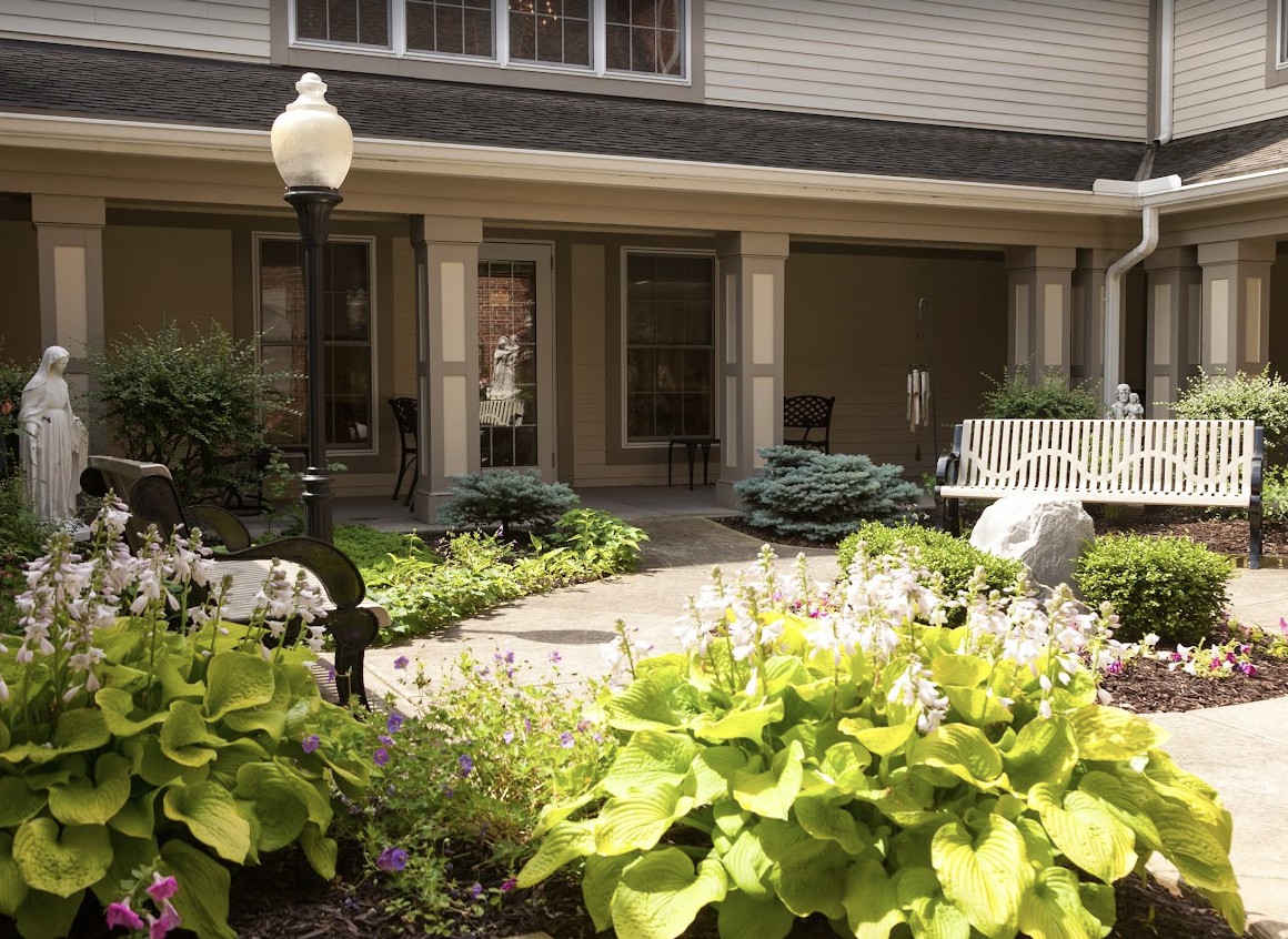 A tranquil courtyard featuring lush greenery, a bench, and a lamp post.