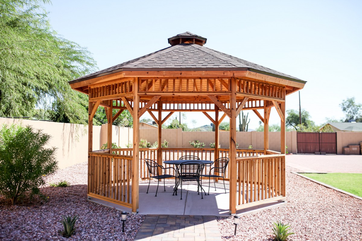 A charming wooden gazebo in a garden setting with patio furniture.
