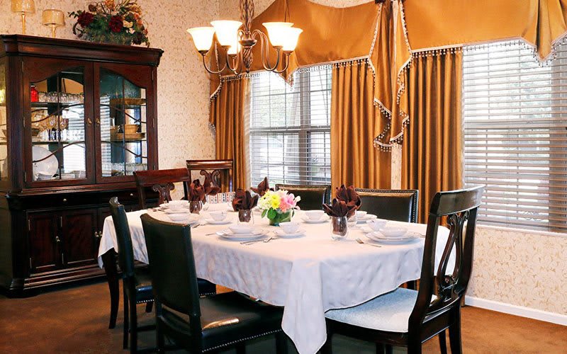 A formal dining room with an elegantly set table, featuring a chandelier and gold curtains.