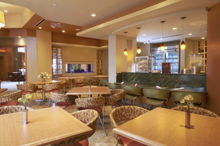 A modern restaurant interior with wooden tables, woven chairs, and warm lighting.