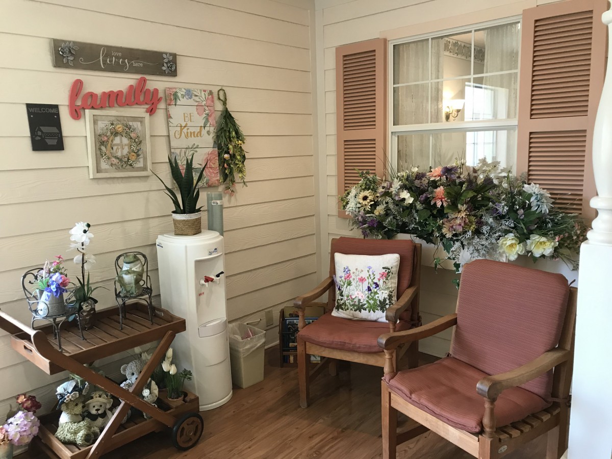 A cozy waiting room featuring two chairs, decorative flowers, indoor plants, and a water cooler.