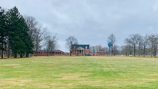 An expansive view of a rural landscape featuring a large house set against a cloudy sky.