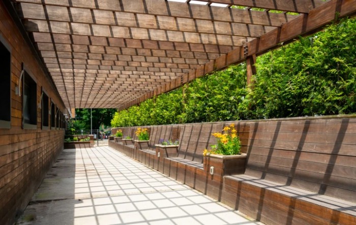 A wooden pergola with seating and planters in an outdoor garden setting.