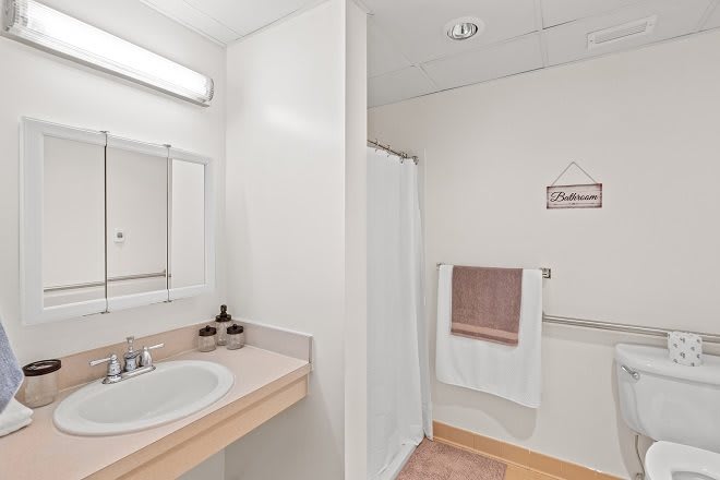 A minimalist bathroom featuring a sink, mirror, and shower area with white walls.