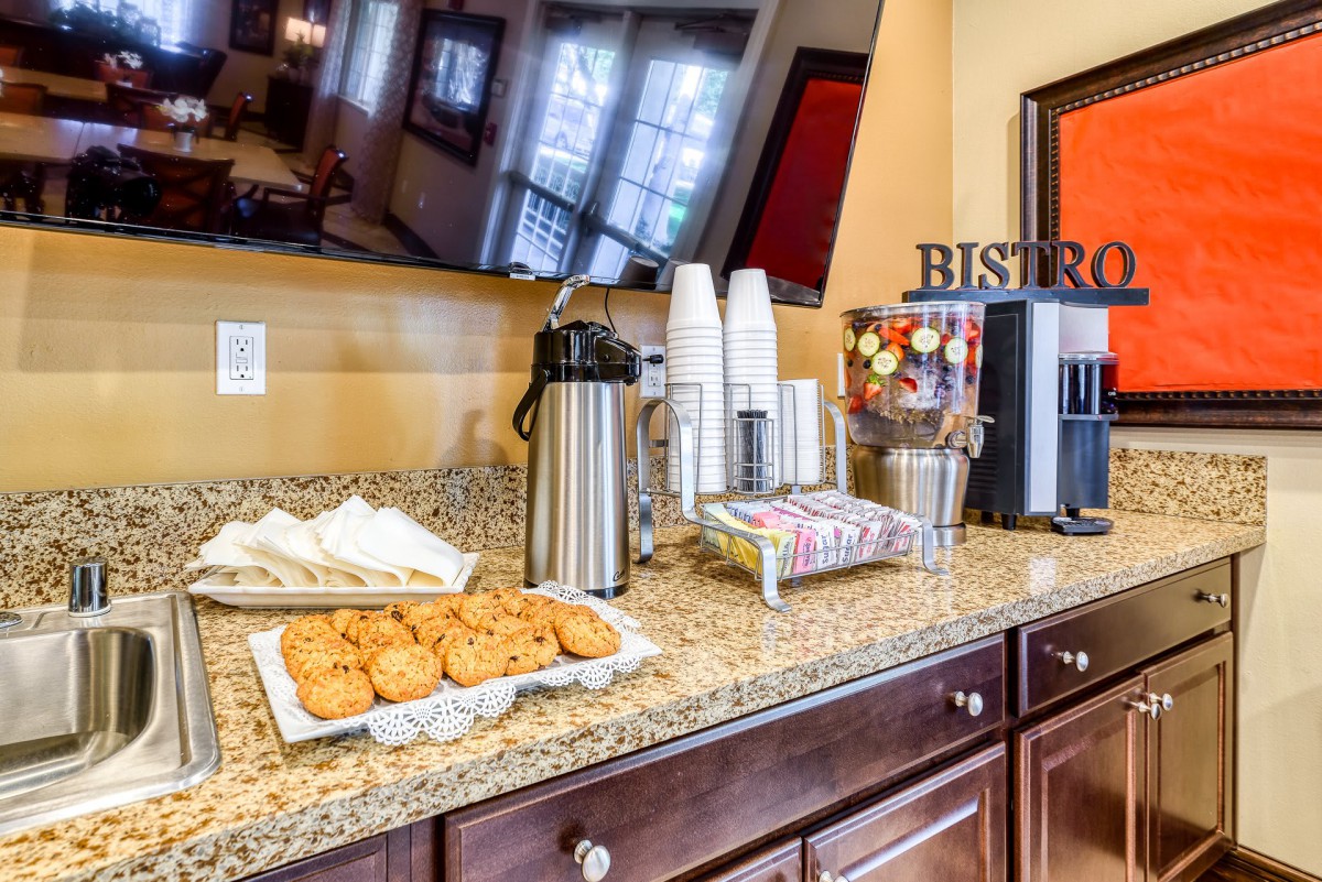 A self-service coffee station with cookies and refreshments on a granite countertop.