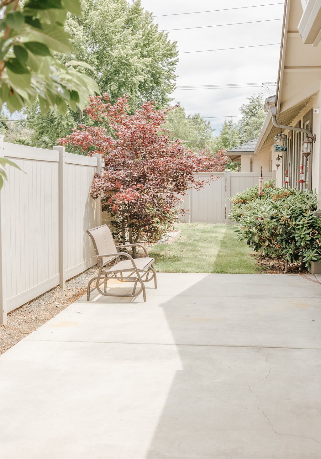 A serene backyard patio with outdoor seating, surrounded by lush greenery and a privacy fence.
