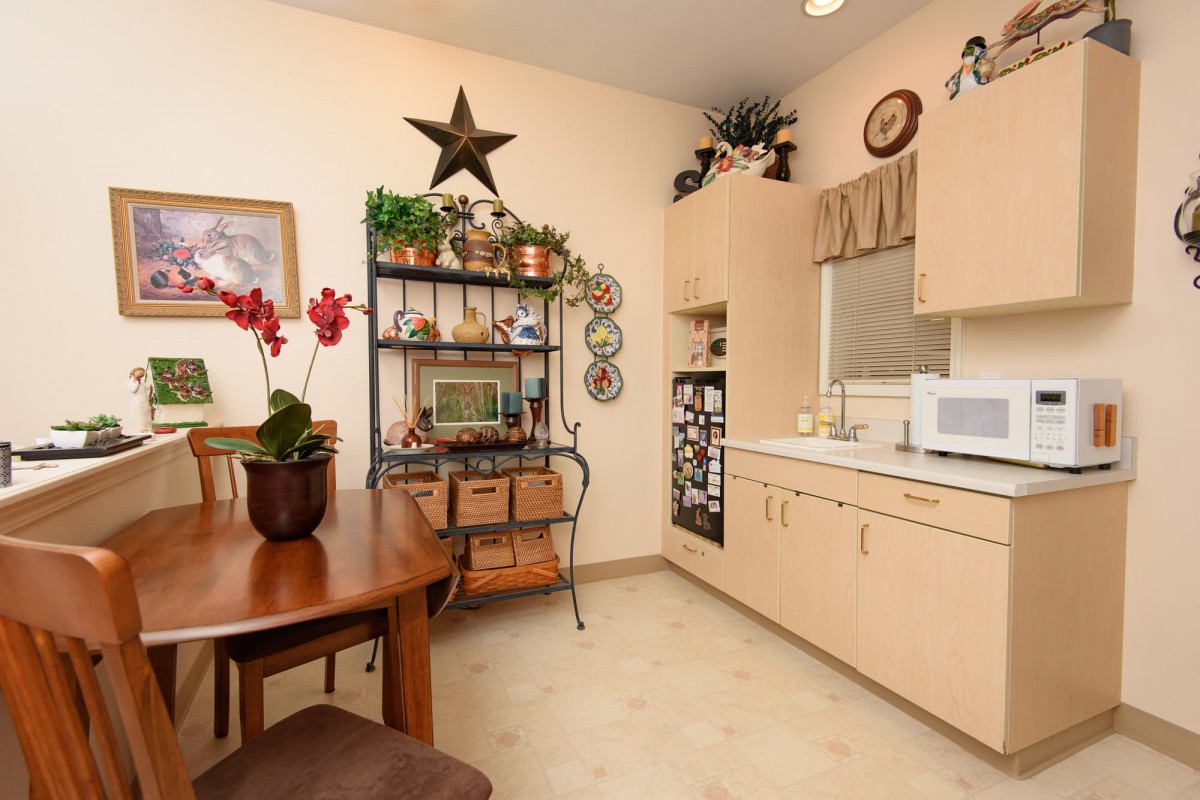 A cozy kitchen corner featuring shelves with plants and decorative items, a wooden table with potted orchids, and built-in cabinetry.