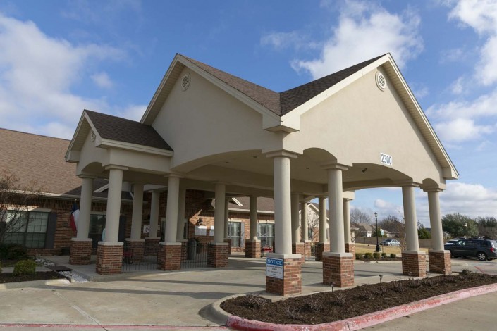 A modern building with a prominent entrance featuring columns and a large overhang on a sunny day.