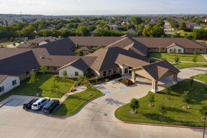 Aerial view of a residential building complex with landscaped surroundings and a parking area.