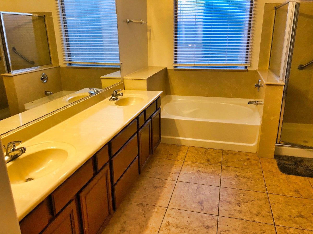 A spacious bathroom with dual sinks, a large mirror, a bathtub, and tiled flooring.