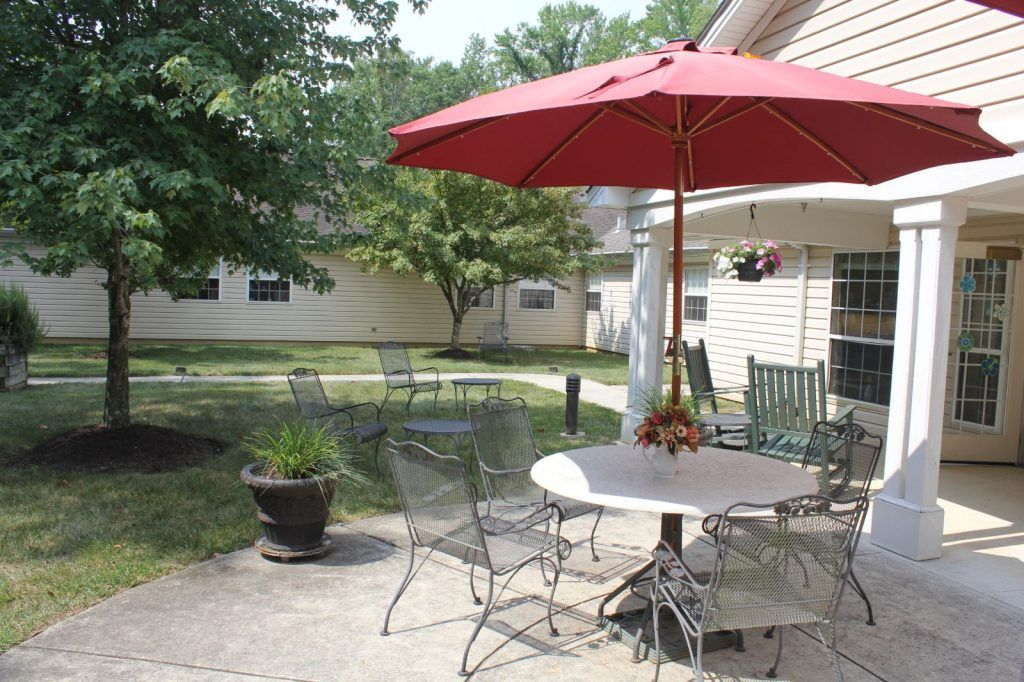 A cozy backyard patio with a red umbrella and outdoor furniture on a sunny day.