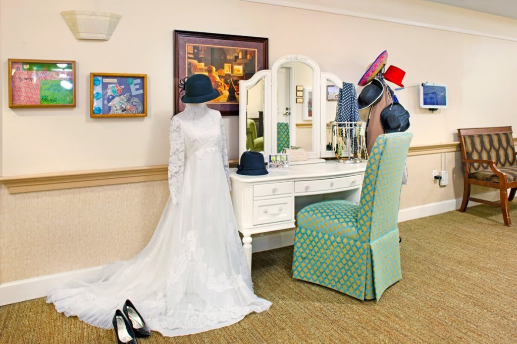 A mannequin dressed in a wedding gown stands beside a vanity table adorned with various hats.