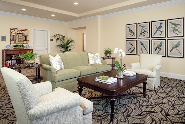 A cozy living room with a green sofa, white armchairs, and a wooden coffee table adorned with decorative items and books.