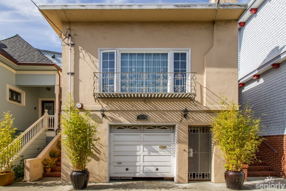 A two-story house with a garage and large windows, flanked by potted plants.