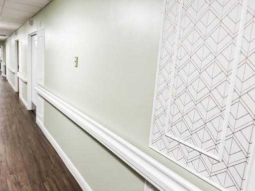 A well-lit hallway featuring green walls, a decorative panel, and wooden flooring.