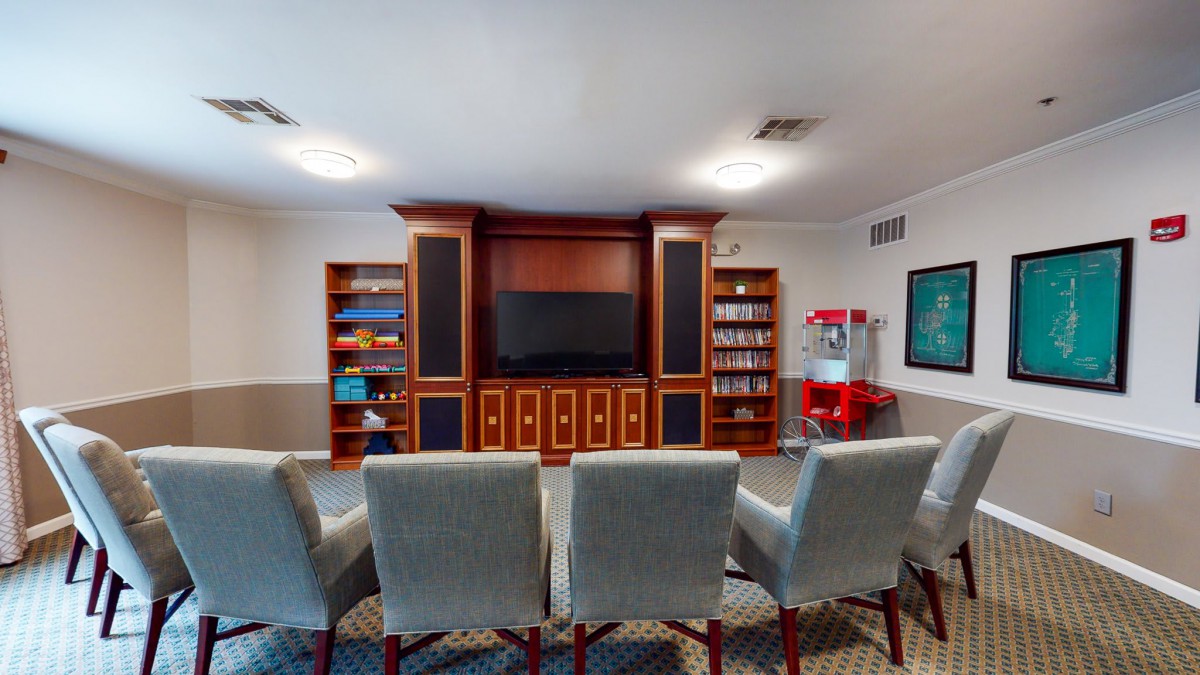 A cozy home theater setup featuring comfortable seating, a large TV, and bookshelves, complete with a popcorn machine for entertainment.