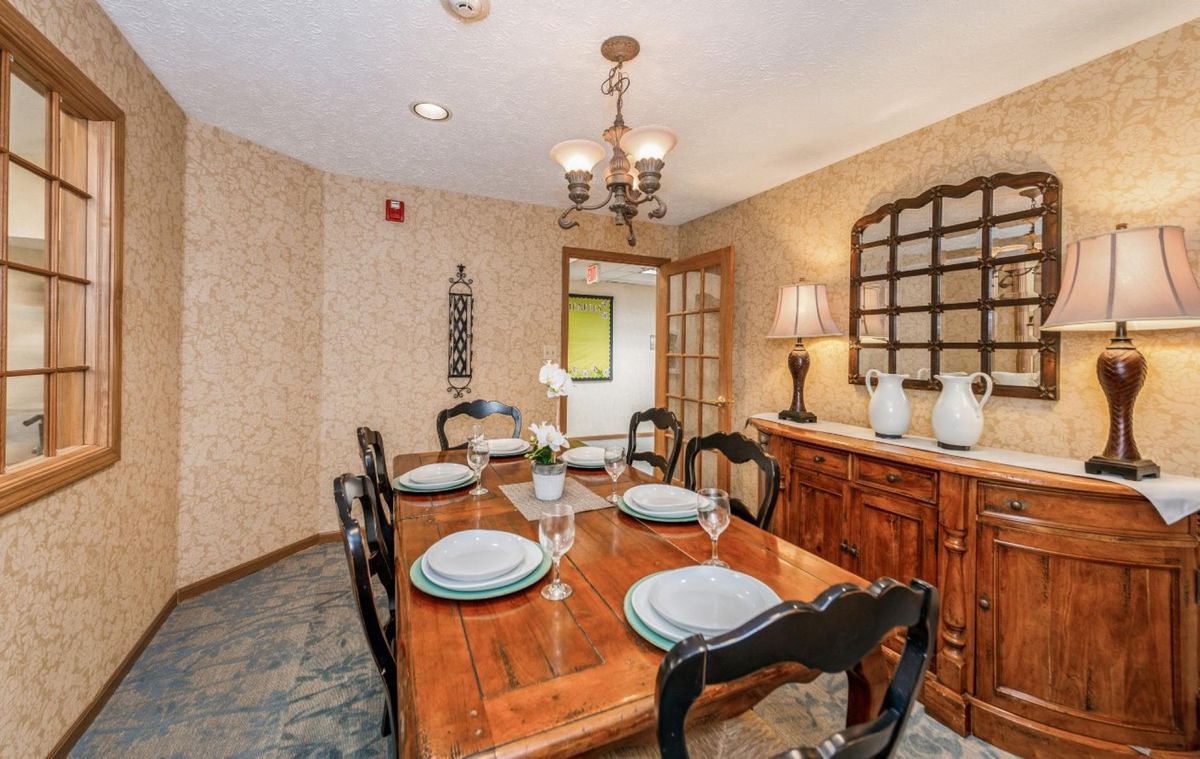 A cozy dining room with a wooden table set for dinner, featuring a chandelier and decorative items.