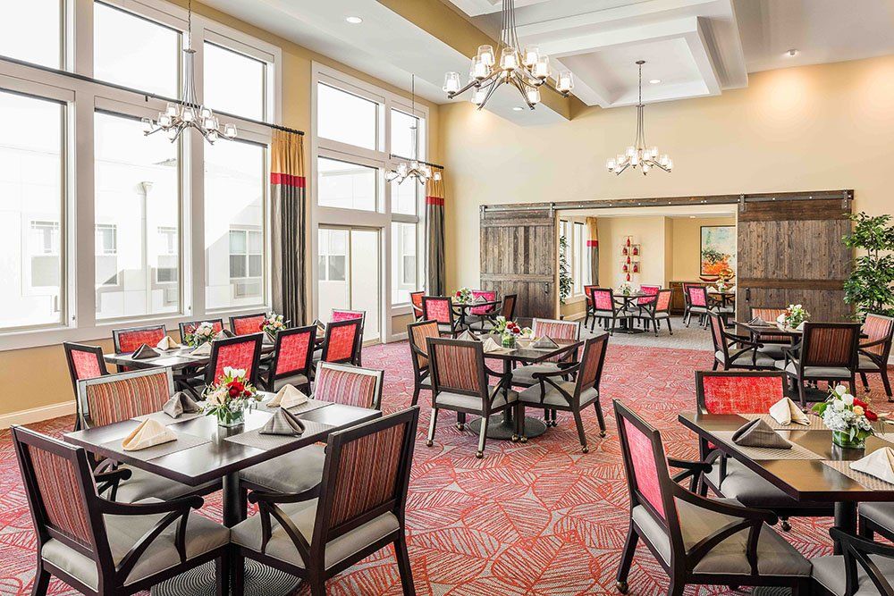 A spacious and elegantly designed dining room with large windows, chandeliers, and well-arranged tables and chairs.