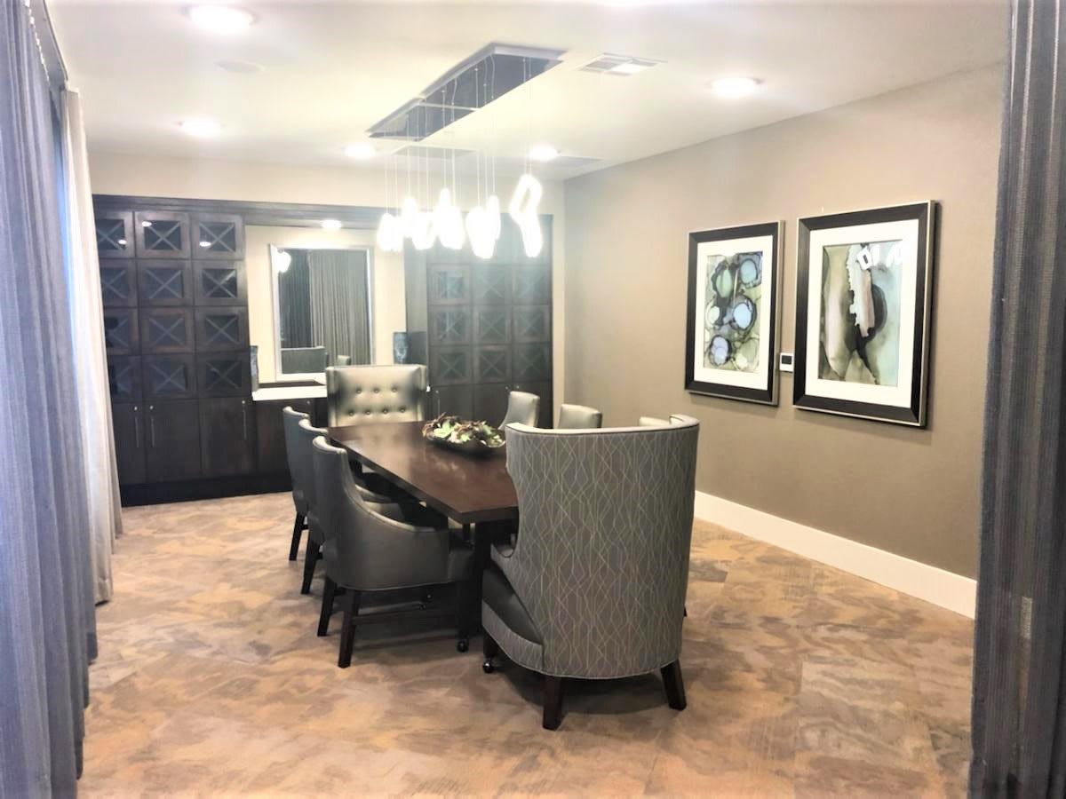 A modern dining room featuring a large table with upholstered chairs, decorative artwork on the walls, and stylish lighting fixtures.