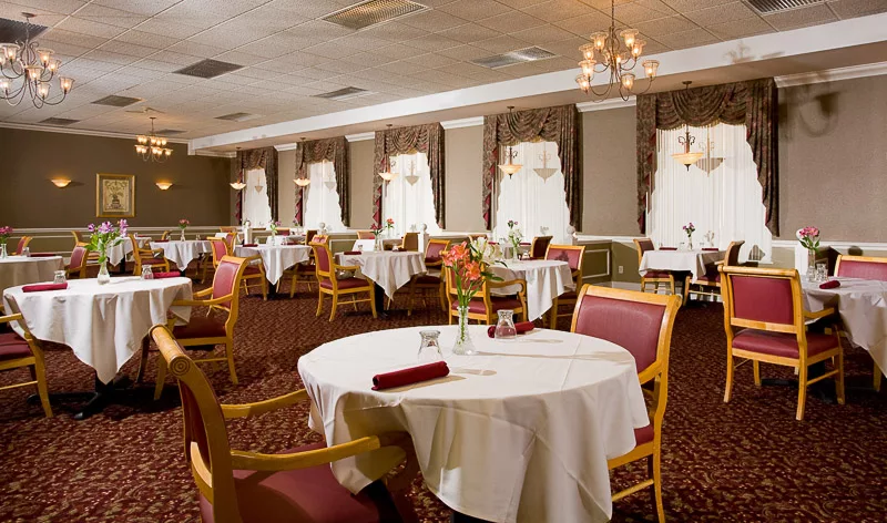 An elegant dining room with neatly arranged tables and chairs, featuring chandeliers and large windows.
