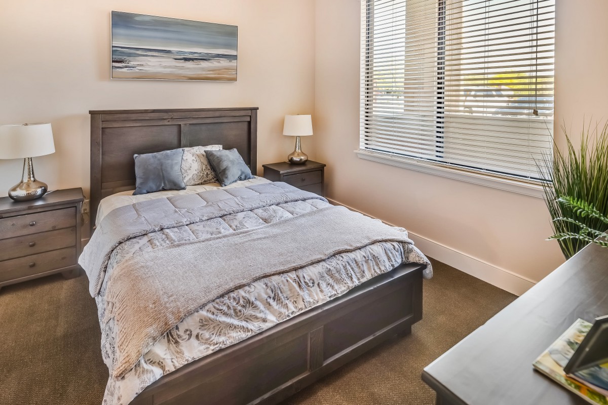 A cozy bedroom with a neatly made bed and a bedside lamp near a window.
