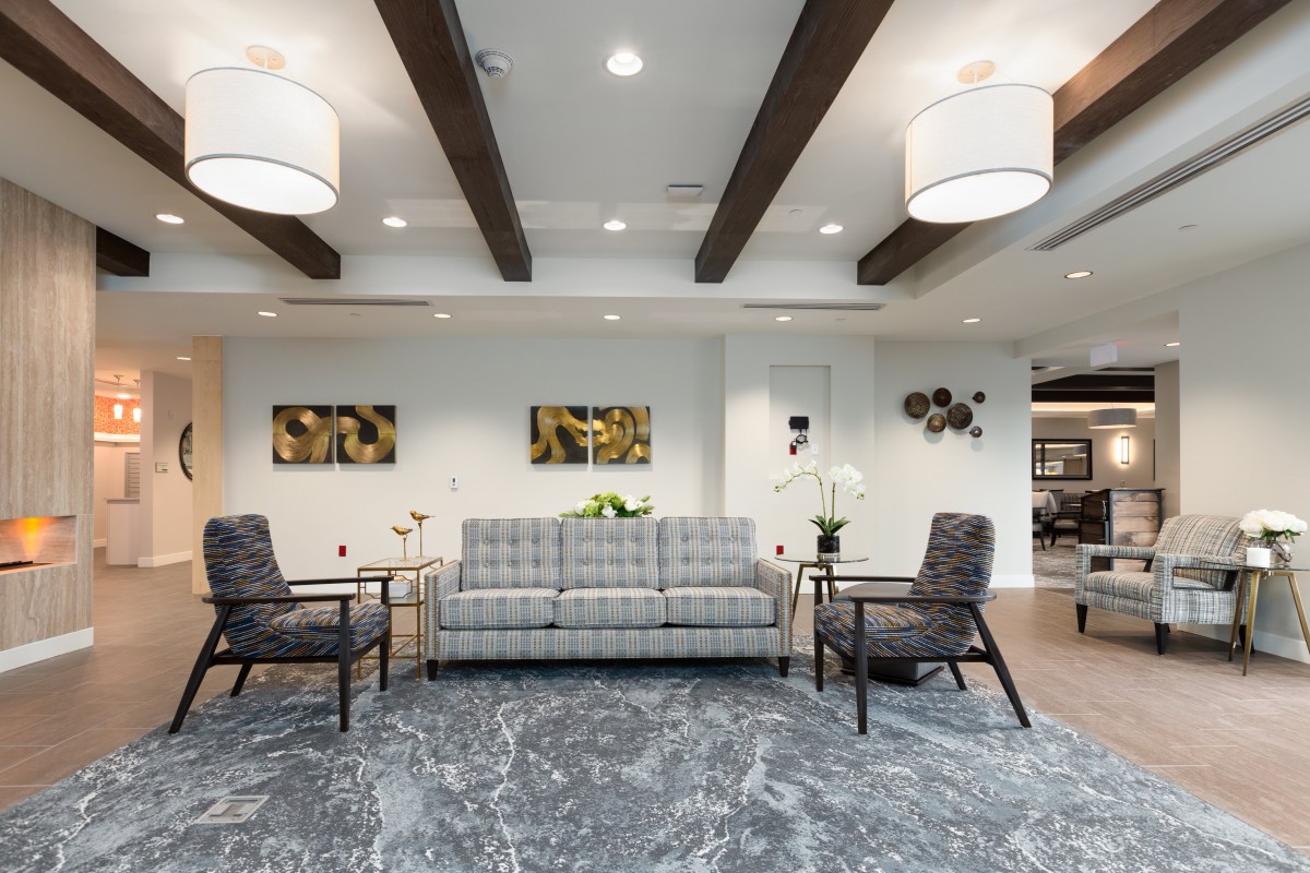 A modern living room featuring a grey sofa, armchairs, and decorative lighting under wooden ceiling beams.