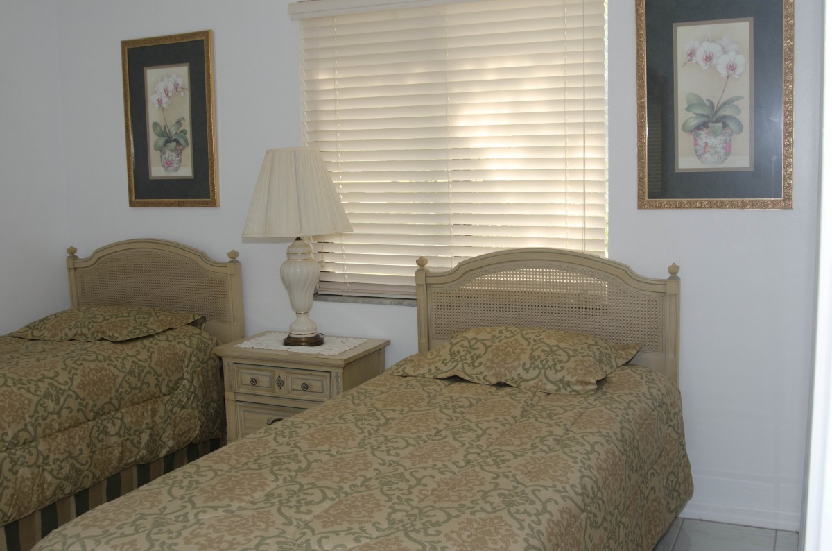 A cozy bedroom featuring twin beds with matching bedding, a central nightstand with a lamp, and framed art on the walls.