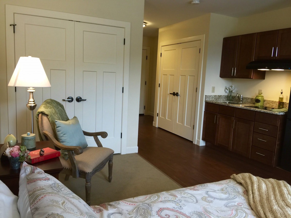 A cozy bedroom with a chair, lamp, and closet, featuring wooden flooring.