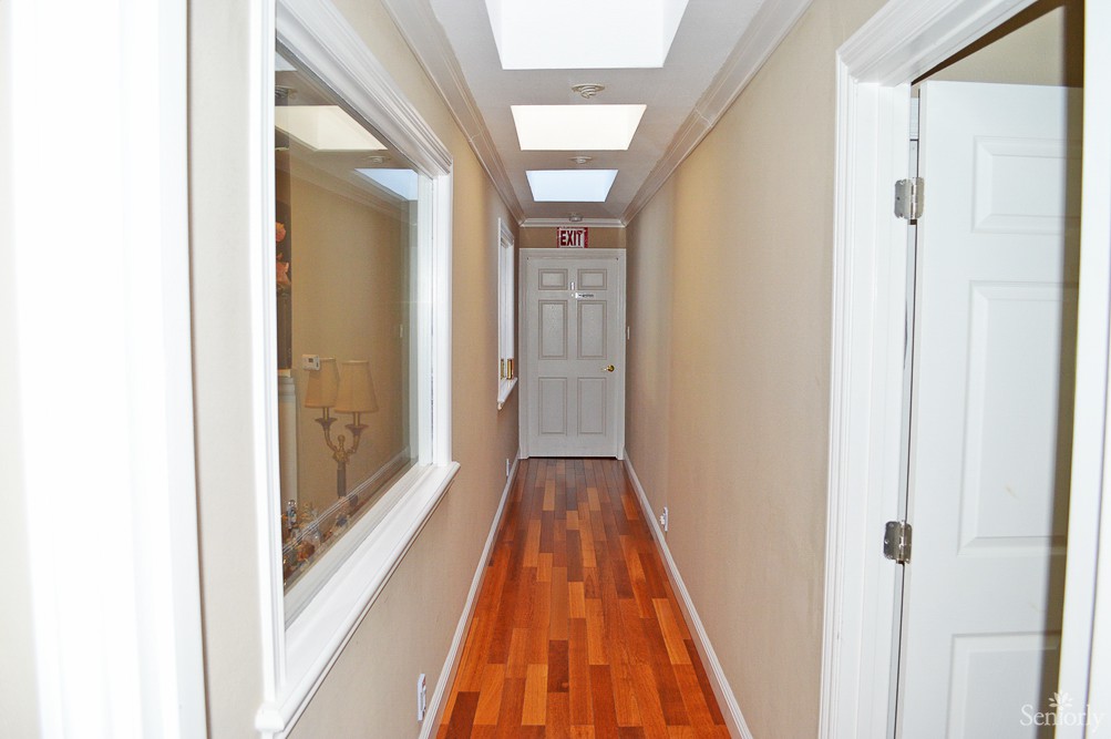 A narrow hallway with wooden flooring, skylights, and a door at the end.