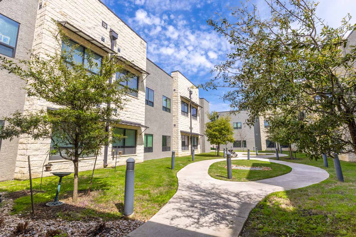 A sunny view of a residential apartment complex with a pathway and green landscaping.