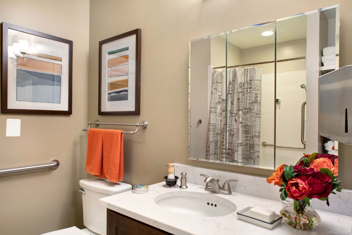A well-organized bathroom featuring a mirror above the sink, orange towels, and decorative wall art.