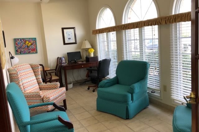 A cozy living room with colorful chairs and a computer desk by the windows.