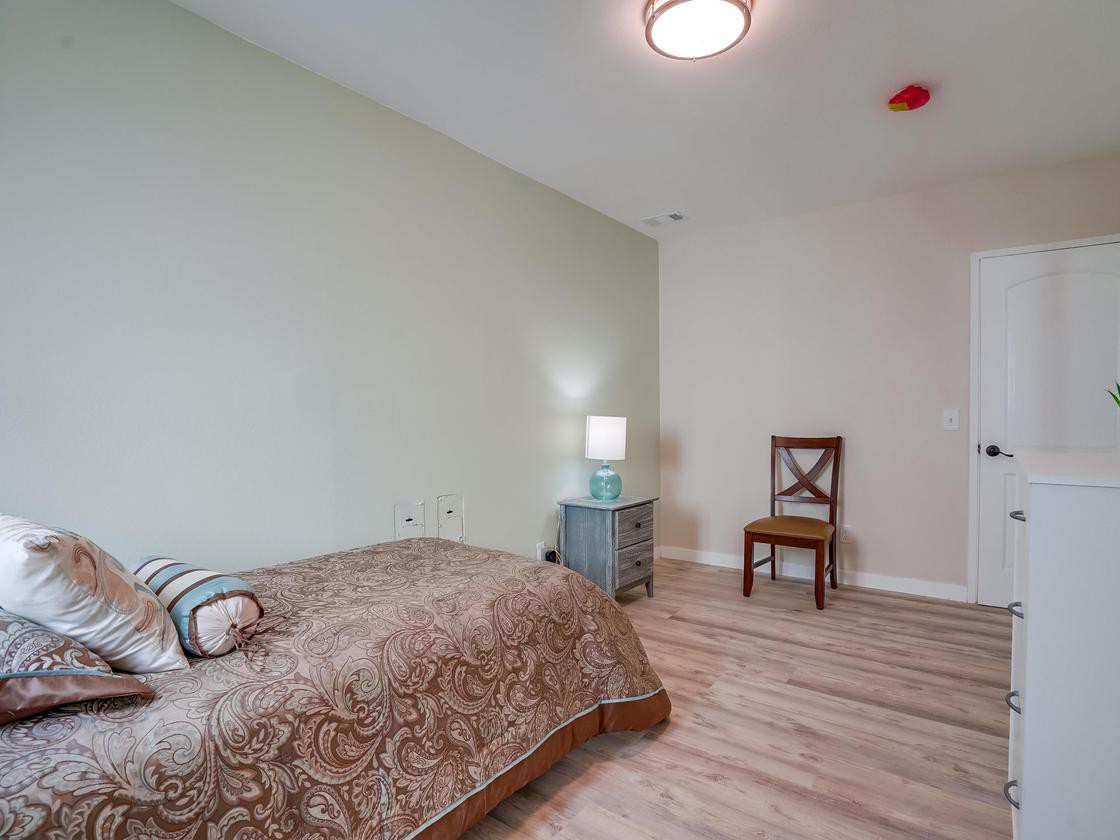 A minimalist bedroom with a single bed, lamp, and chair on wooden flooring.