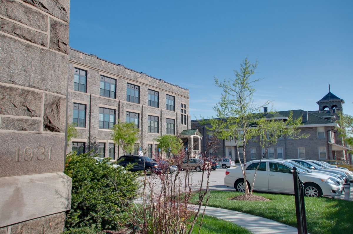 A view of a residential building with parked cars along a street lined with trees.