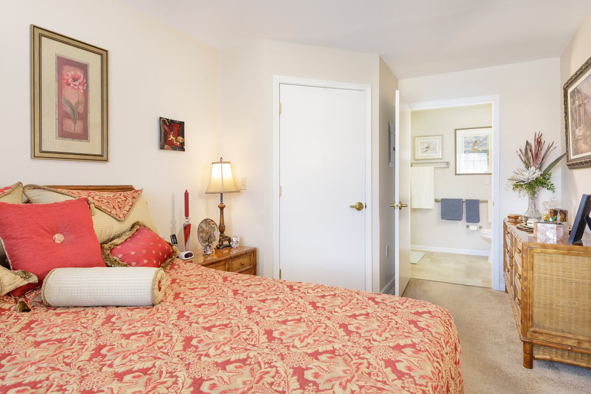 A cozy bedroom featuring a patterned bedspread, nightstand with a lamp, and an open view into a bathroom.