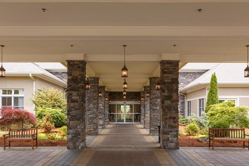 A covered entrance with stone pillars leading to a building, surrounded by landscaped greenery.