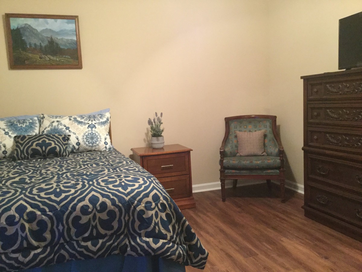 A cozy bedroom with a bed, nightstand, chair, and dresser.